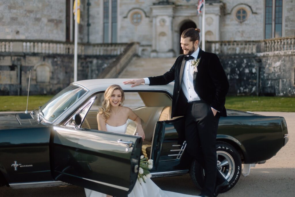 Wedding couple sit by vintage car at their London Wedding with castle in background