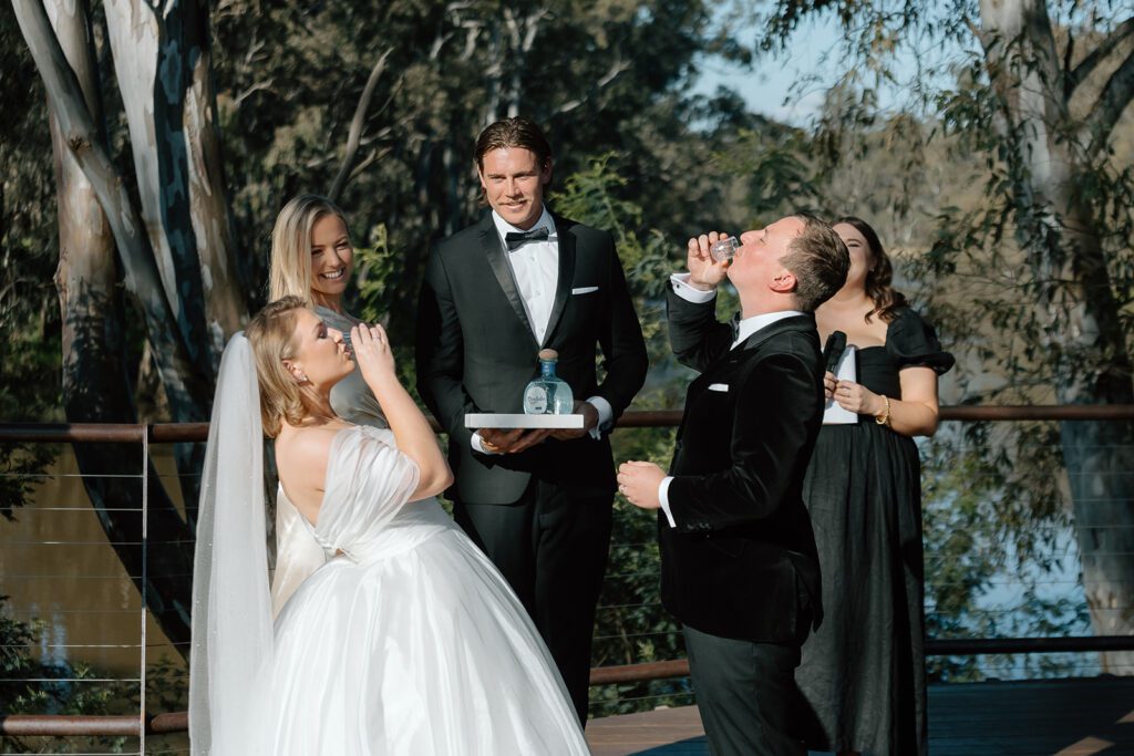 A bride and groom shot Don Julio Tequila as part of their unity shot in the middle of their wedding ceremony. Their celebrant, groomsman and bridesmaid stand behind them smiling.